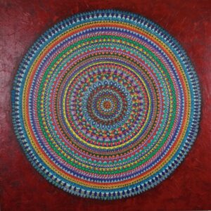 The Sacred Circles, a vibrant circular mandala artwork featuring intricate concentric rings of geometric and floral patterns in blue, green, yellow, pink, orange and purple, set against a textured deep red background.